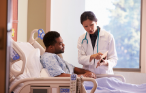 Hospital Doctor With Digital Tablet Talks To Male Patient