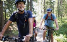 Two people smiling while riding bikes in the forest 